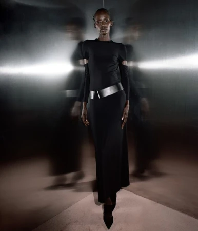 Elegant Black woman in a black gown with a metallic belt stands against a dark, reflective background, showcased with creative motion blur.