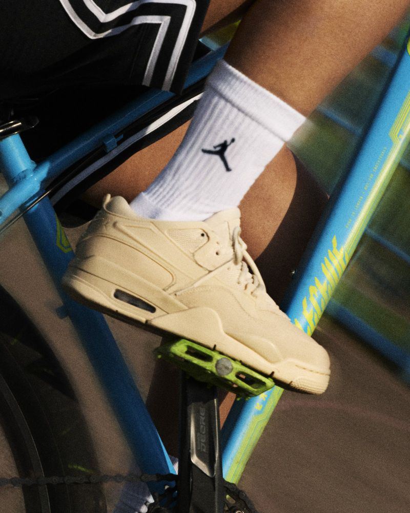 Close-up of a cyclist's tan sneaker on a green pedal of a light blue bicycle, complemented by white Jordan socks, and black shorts.