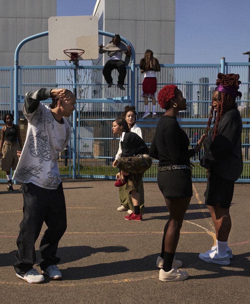 Outdoor scene with diverse group of young adults on a basketball court in casual street style, with building and blue sky in background.