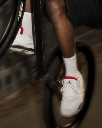Close-up of a person riding a bike wearing white and red sneakers, emphasizing footwear and active lifestyle. Focus is on motion and style.