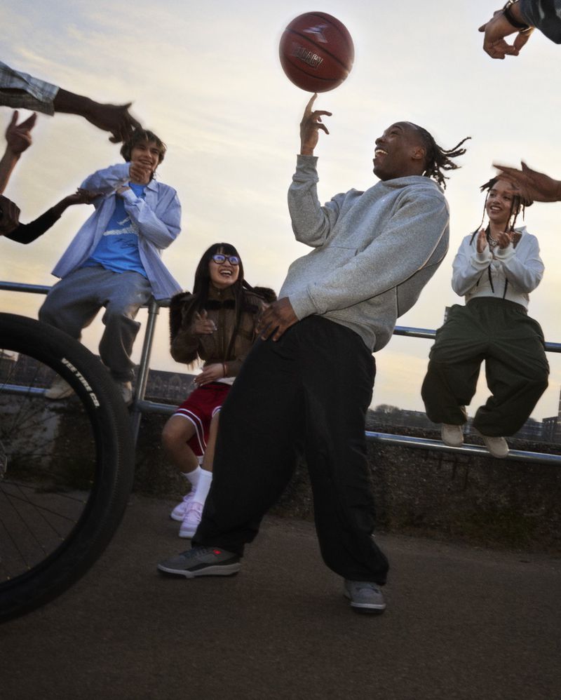 Group of young adults outdoors with a man spinning a basketball on his finger, showcasing a casual and active lifestyle.