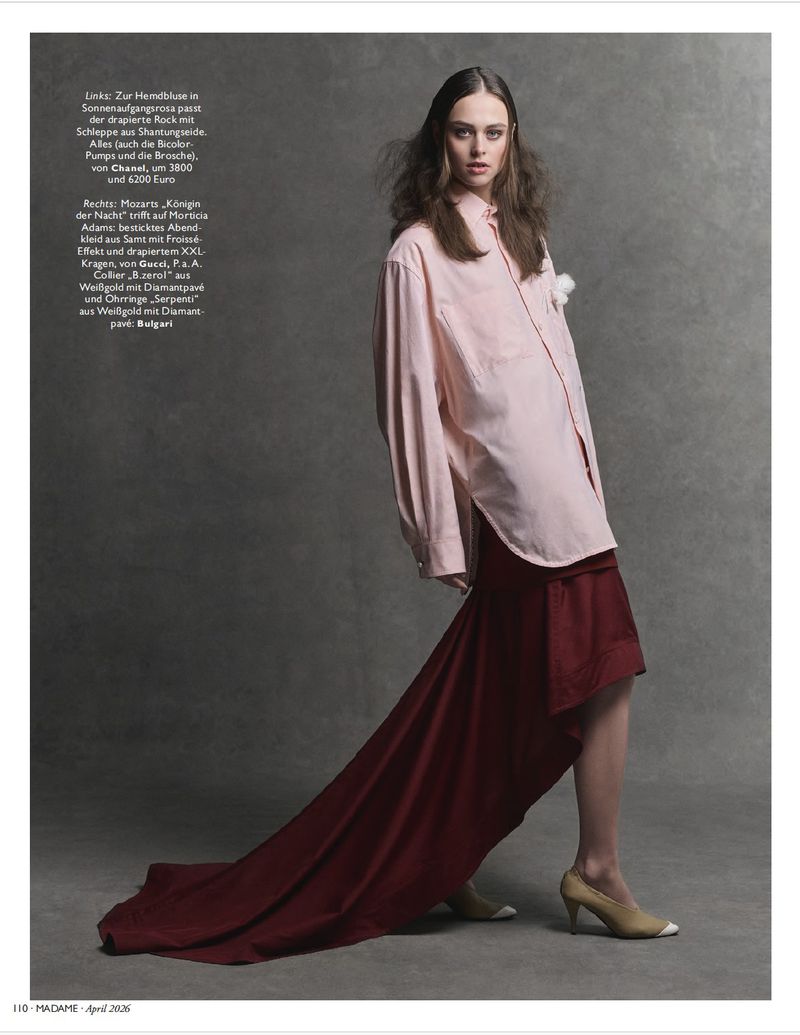Model wearing an oversized pink shirt and long red draped skirt against a textured grey background.