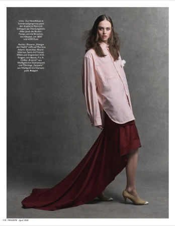 Model wearing an oversized pink shirt and long red draped skirt against a textured grey background.