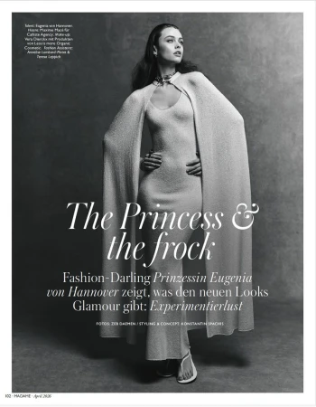 Model wearing a long cream knit dress with a matching cape posed against a mottled textured studio backdrop.