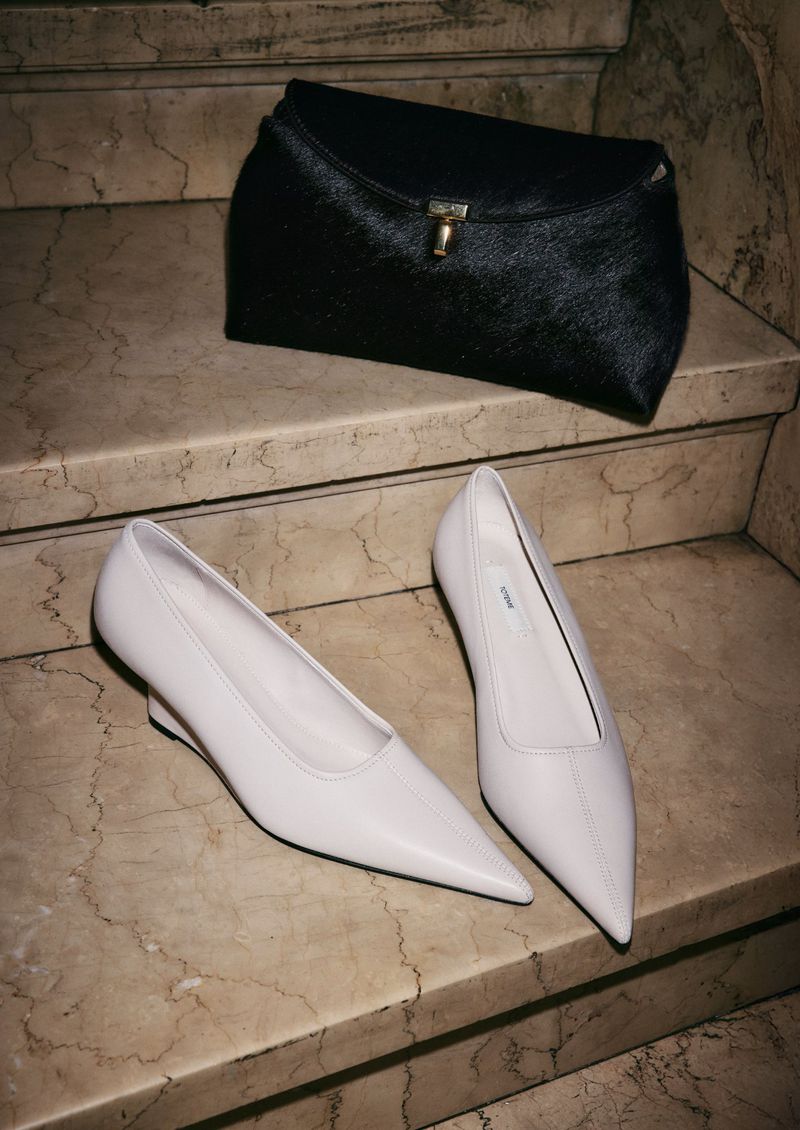 Fashionable still life on marble steps showcasing white pointed-toe pumps paired with a black fur clutch for a sophisticated look.