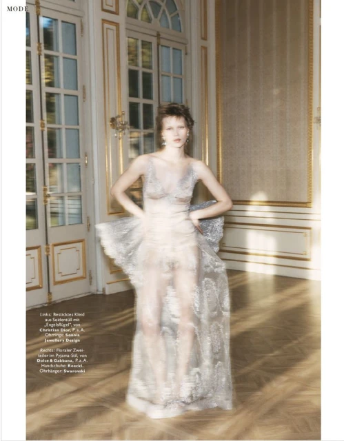 Fashion editorial shot of a woman in a sheer embellished gown posing in an ornate interior with gilded moulding and natural light.