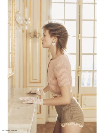 Model in pink knit cardigan and shorts wearing lace gloves standing in an ornate room