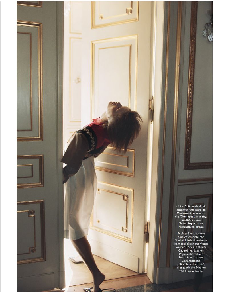 Model with short hair leaning back in a doorway while wearing a white skirt and a black and red top in a classic architectural interior.