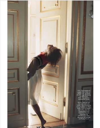 Model leaning backward through a doorway in a white dress with red top, framed by ornate classic white and gold paneled doors.