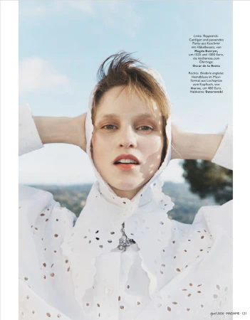 Model wearing a white embroidered blouse and hood outdoors against a blue sky