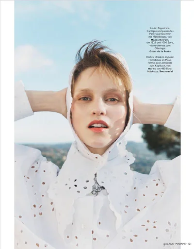 Model wearing a white embroidered blouse and hood outdoors against a blue sky