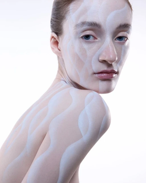 Artistic portrait of an adult female with face and body paint in white, posing in front of a white background.