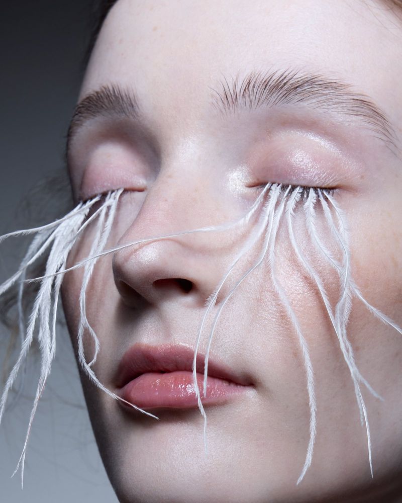 Close-up beauty shot of a fair-skinned model with closed eyes and white feathered eyelashes. Beauty and Fashion imagery.
