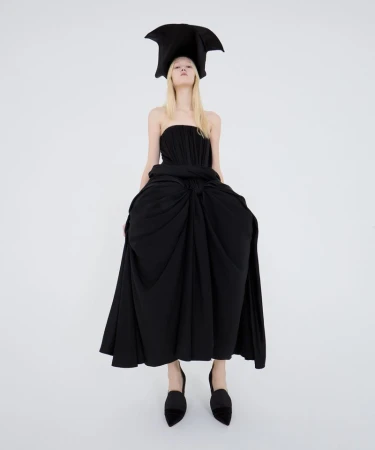 Model in a sculptural black dress and matching horned hat against a clean white backdrop for T Magazine China special.