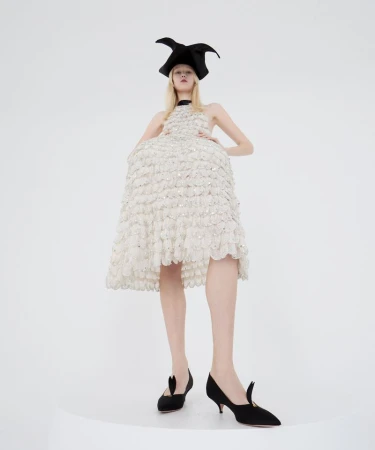 Model wearing a textured white dress and black horned hat against a white seamless background