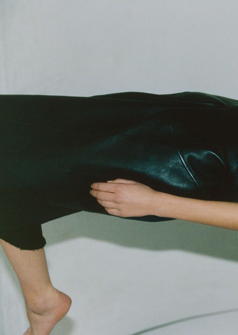 Close-up studio shot of a person's bare foot, leg, hand, and partially visible torso against a white background, emphasizing skin tones.