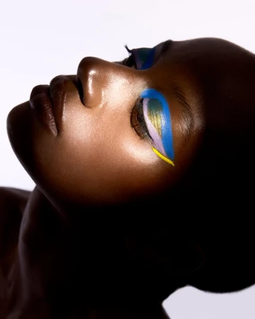 Close-up of an African-American woman with colorful makeup on her closed eye. The woman is in a photo studio environment.