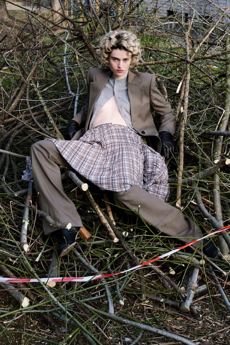 Fashionable young adult in couture outfit poses in a pile of tree branches in an outdoor setting under natural daylight.