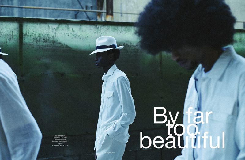 Three African-American men in white clothing and hats stand against a textured wall, bathed in cool-toned light, presenting a fashion editorial.
