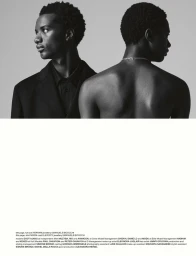 Black-and-white portrait of two men, one in a black blazer and shirt, and another shirtless from behind with a silver necklace.