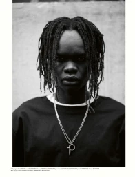 Black and white portrait of a model with dreadlocks wearing a dark crewneck t-shirt with layered silver necklaces.