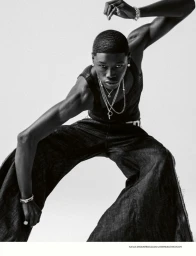 Black male model in dark tank top and wide-cut trousers posing against white background for Num&eacute;ro Homme Switzerland.