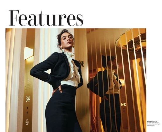 Model in black blazer and ruffled white blouse posing next to a mirrored elevator door for Modern Luxury