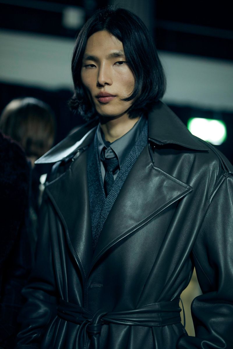 A sleek, gray-toned fashion shot features an Asian adult male in a stylish, belted leather trench coat, capturing a modern, elegant aesthetic.