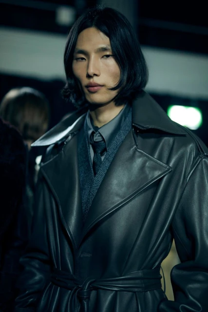 A sleek, gray-toned fashion shot features an Asian adult male in a stylish, belted leather trench coat, capturing a modern, elegant aesthetic.