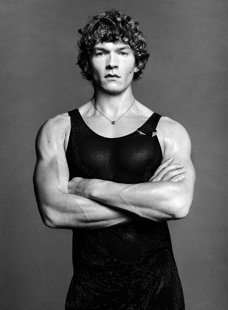 Portrait of Connor Storrie with curly hair wearing a black tank top and necklace with arms crossed