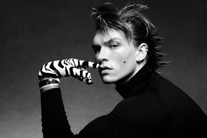 Monochrome portrait of a male model wearing a black turtleneck, a zebra-print glove, and bracelets against a dark background.