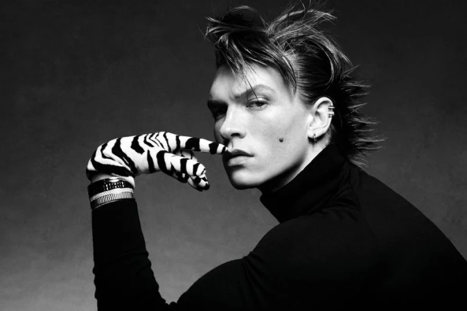 Monochrome portrait of a male model wearing a black turtleneck, a zebra-print glove, and bracelets against a dark background.