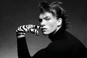 Monochrome portrait of Connor Storrie wearing a dark turtleneck and zebra-patterned gloves against a grey background.