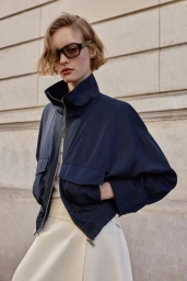 Model wearing a dark blue zip-up jacket and sunglasses against a stone building exterior for Zara Woman March 2026.