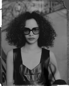 Model wearing dark sunglasses and a black leather top with voluminous dark curly hair in a portrait shot by Gus Van Sant for Celine