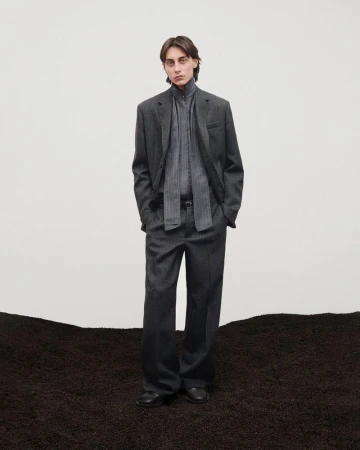 A man in a dark grey suit standing on a textured dark mound against a plain white studio background.