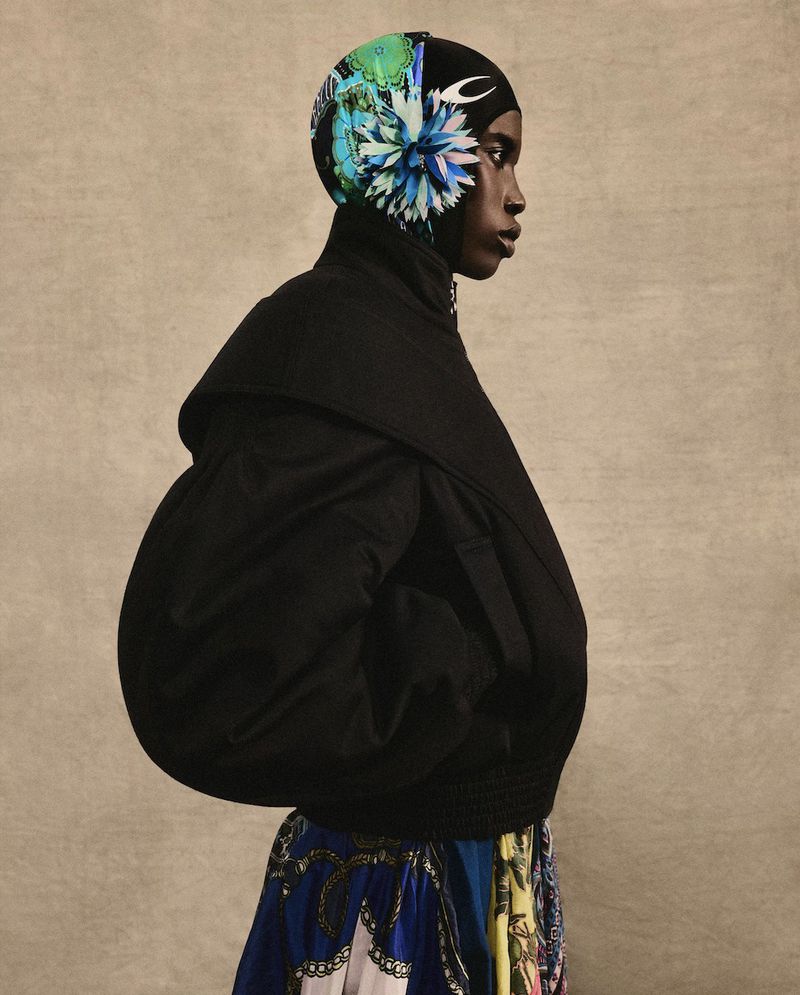 Profile shot of an African-American woman wearing a patterned headscarf and black jacket against a neutral backdrop in a studio.
