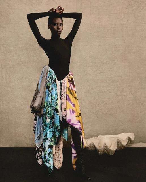 Fashionable woman poses in black bodysuit and scarf skirt against neutral backdrop. Studio shot, portrait, full-length.