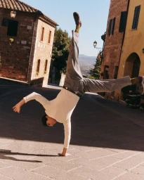 Man doing a handstand on a cobblestone street lined with traditional buildings during SS26 for Paul Smith