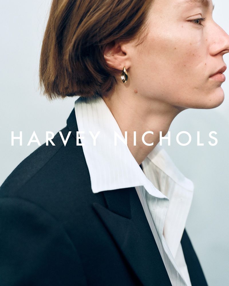 Profile portrait of a short-haired model wearing a black blazer, white shirt, and gold earring for Harvey Nichols.