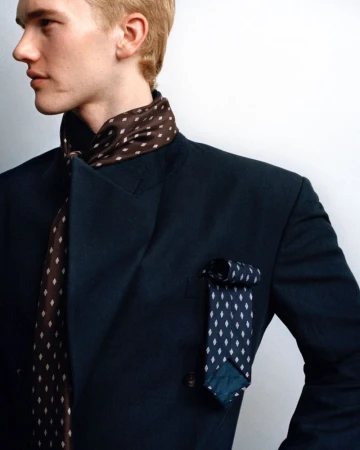 Male model in navy blue jacket with patterned ties. Fashion-forward styling against a clean white backdrop in a studio setting.