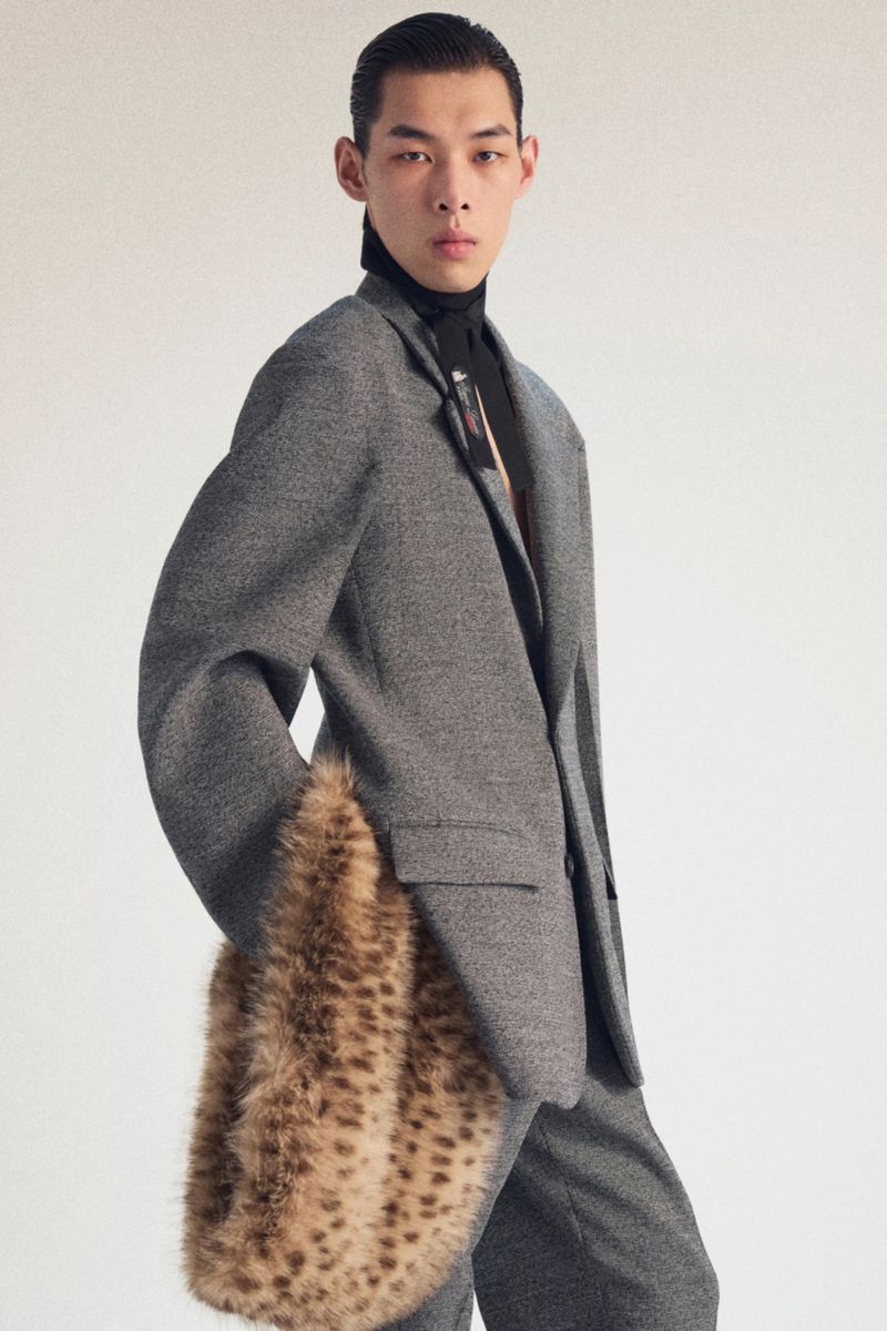 Male model in gray suit with fur muff. Studio shot highlighting men's fashion, clothing, and modern style against a neutral backdrop.