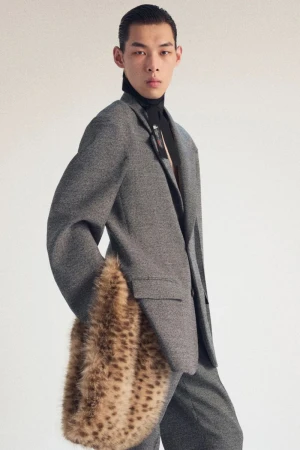 Male model in gray suit with fur muff. Studio shot highlighting men's fashion, clothing, and modern style against a neutral backdrop.