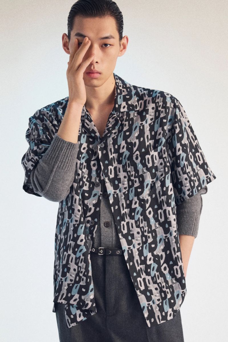 Model in printed short-sleeve shirt and grey layered sweater against a white seamless background