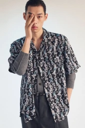 Model in printed short-sleeve shirt and grey layered sweater against a white seamless background