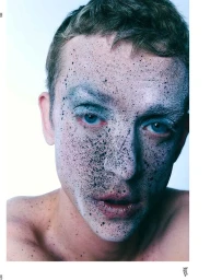 Close-up portrait of a young man with white powder and dark speckles on his face against a white background