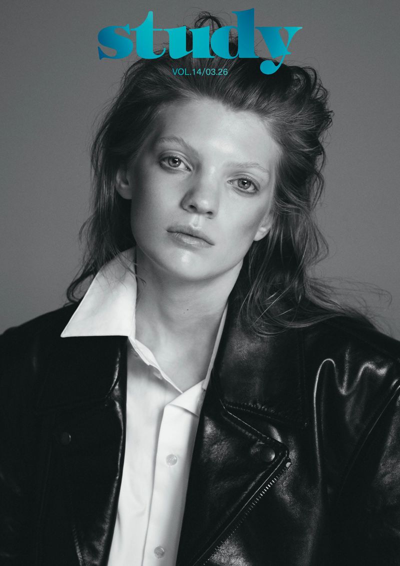 Black and white magazine cover featuring a model in a black leather jacket and white collared shirt against a gray backdrop.