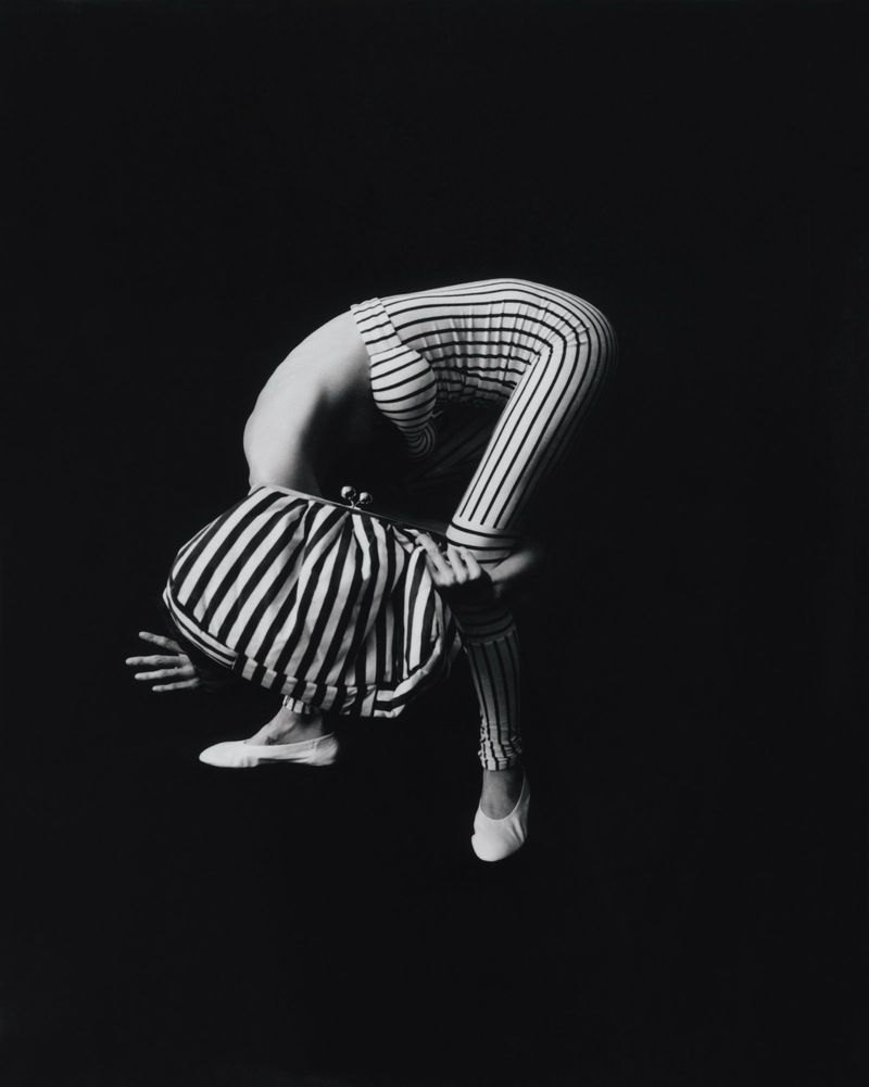 Black and white photograph of a person wearing striped clothing, bending over with one hand on the ground and wearing white shoes.