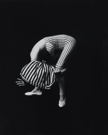 Black and white photograph of a person wearing striped clothing, bending over with one hand on the ground and wearing white shoes.