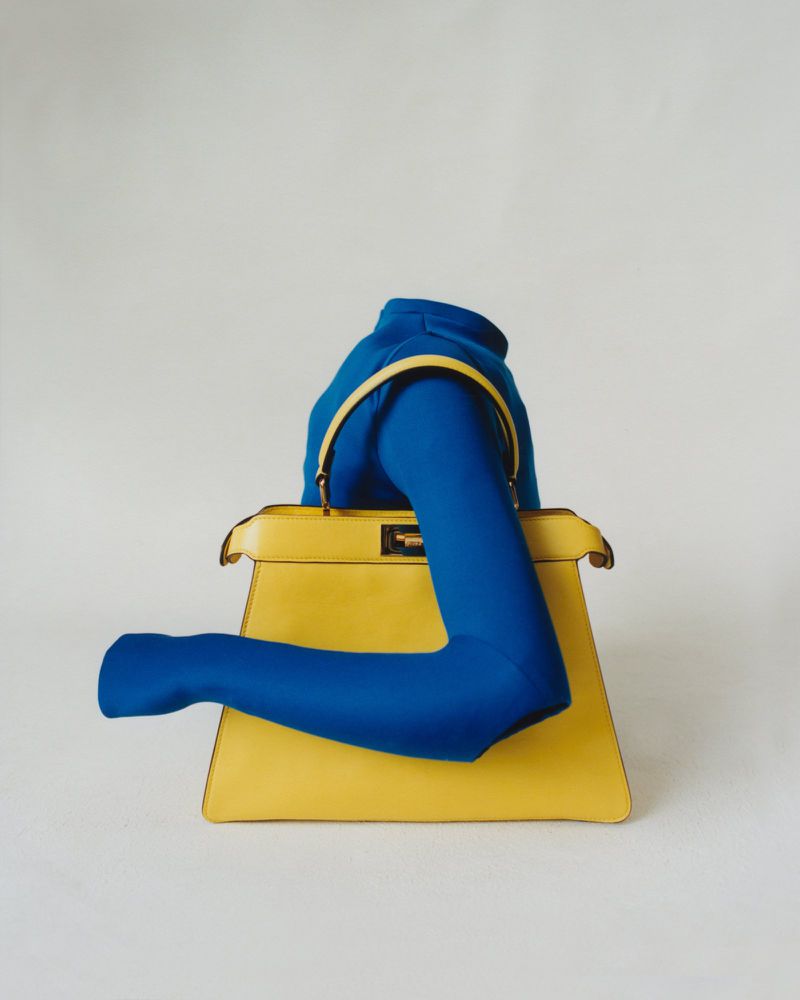 Fashion still life of a yellow handbag featuring a model's arm draped over it, set against a clean, minimalist white backdrop.